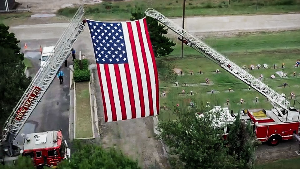 Lake Ridge Chapel Graveside service honoring fireman with large American flag hoisted on truck ladders